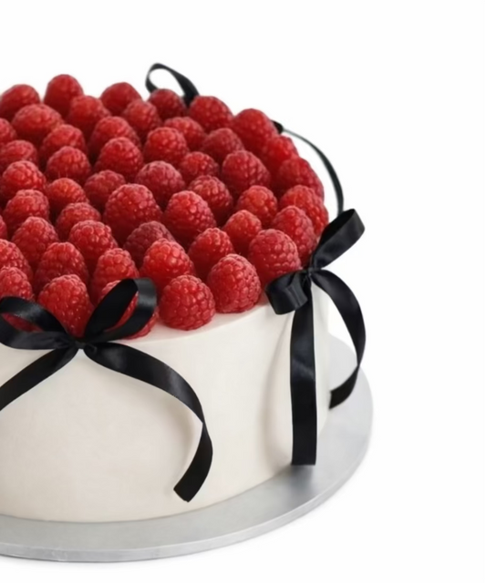 Cake decorated with raspberries and black ribbons on a white background
